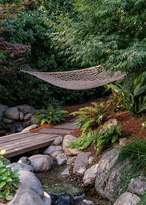 hammock in lush garen next to creek and bridge