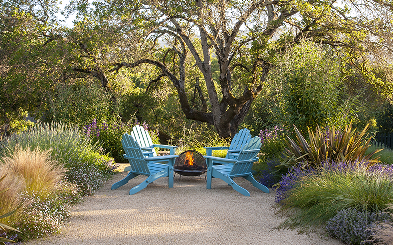 wildflower meadow and grasses around a backyard fire pit with four blue adirondack chairs