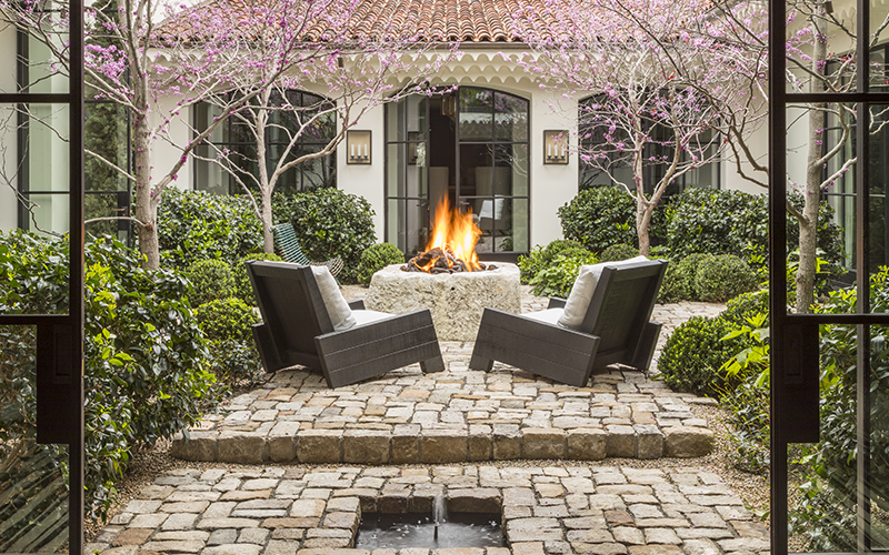 a tranquil garden scene with outdoor chairs under flowering redbud trees and around a firepit