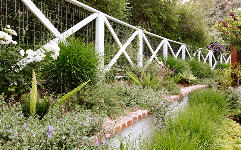 white fence with green landscaping on retaining wall