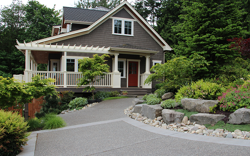 driveway up to gray house with green landscaping