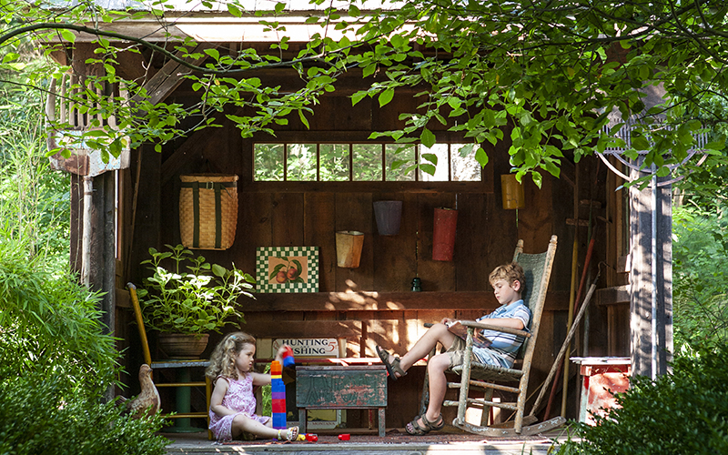 children playing in a wood playhouse with trees and greenery surrounding it