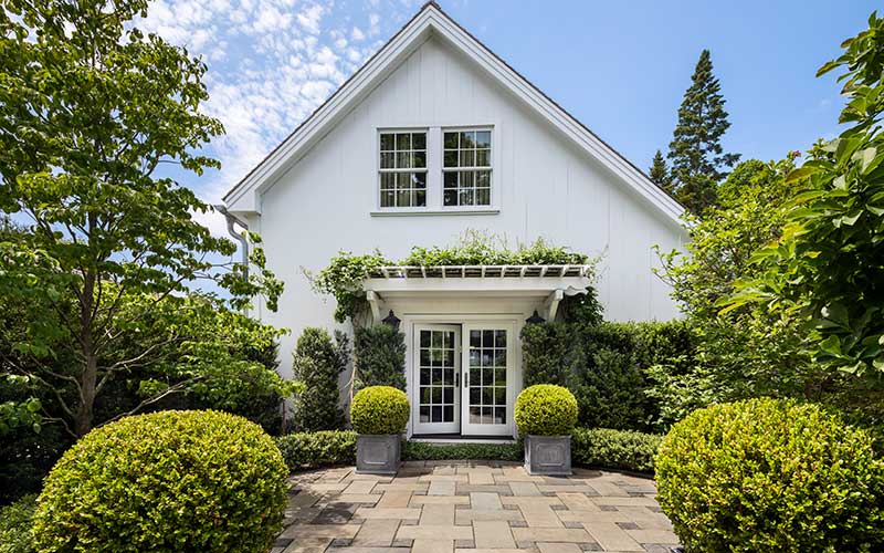 boxwoods and clematis in formal garden in front of white house