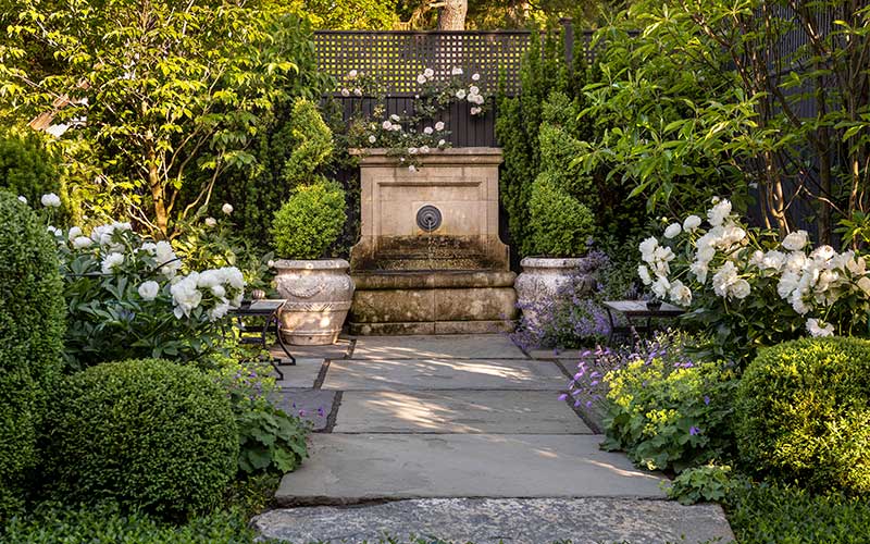 fountain in formal garden with peonies and boxwoods
