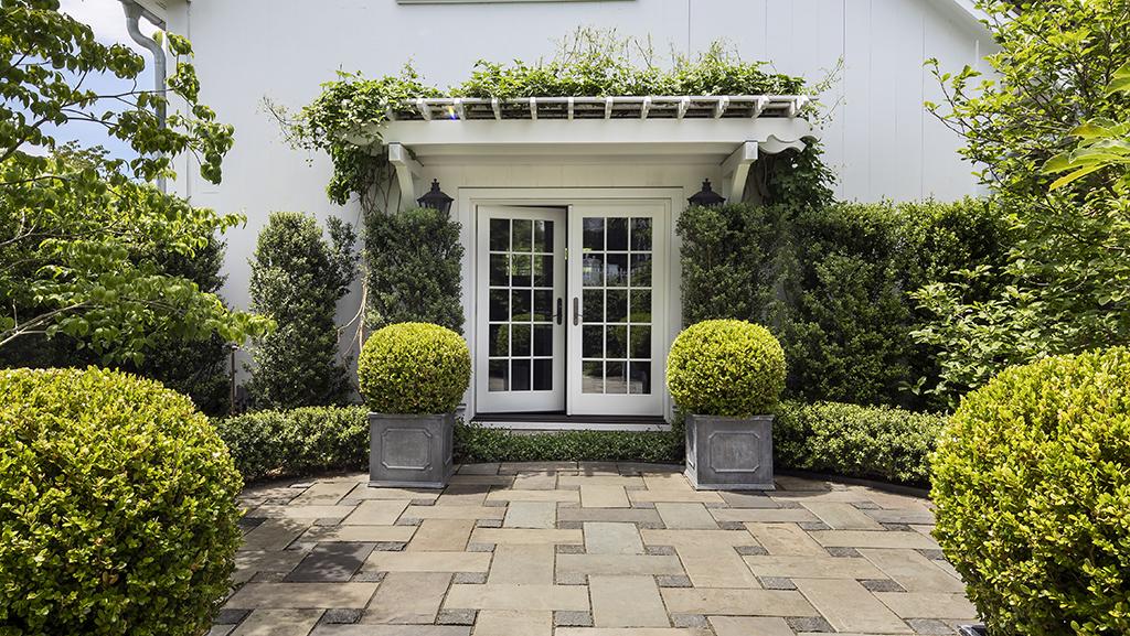 shaped boxwoods in containers and hedges in front of white house with French doors
