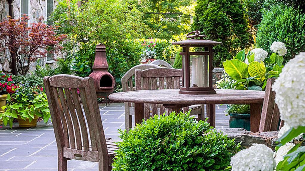 Patio with a wooden table and chairs surrounded by hydrangeas for privacy, boxwood, a Japanese maple and annuals.
