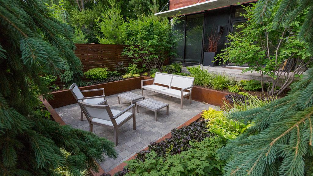 Tiny backyard landscape with patio furniture in the center and filled with evergreens, conifers, and shade-loving perennials.