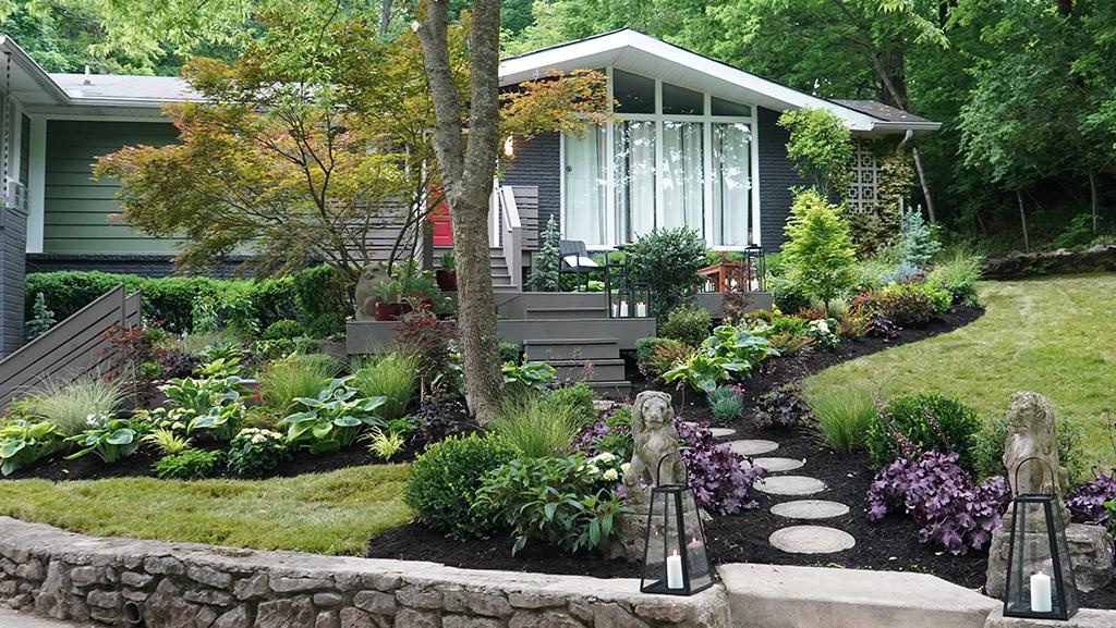 Landscape in back of home with stone pathway and plants like Amethyst Heuchera, Viburnum, hosta, Hydrangeas, and tall grass. 
