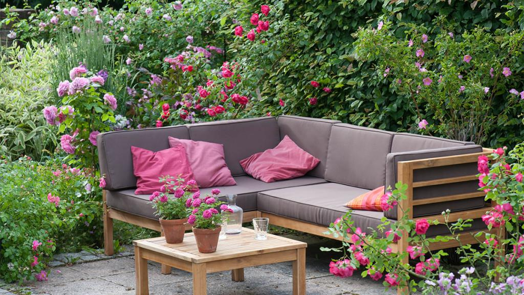 Outdoor couch furniture surrounded by a variety of pink and violet flowers including roses.