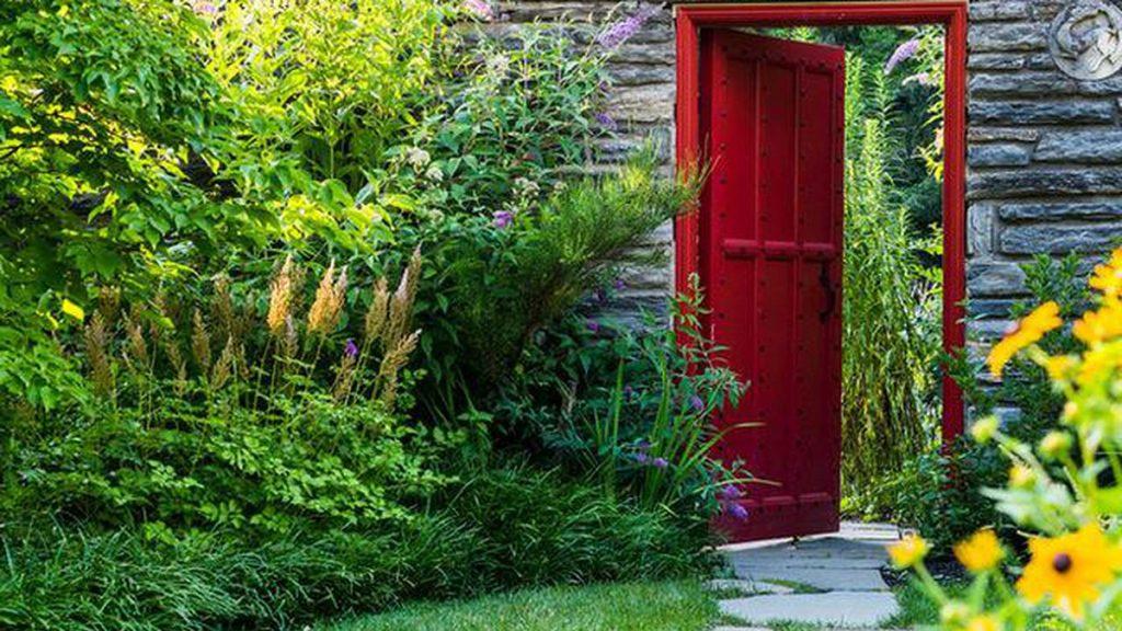 Garden scene of different green bushes and trees leading up to a red door.