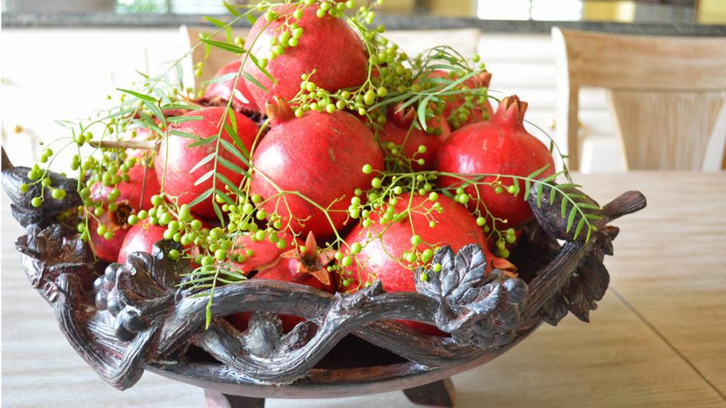 A bowl full of pomegranates and unripened California pepperberry for decoration on a table.