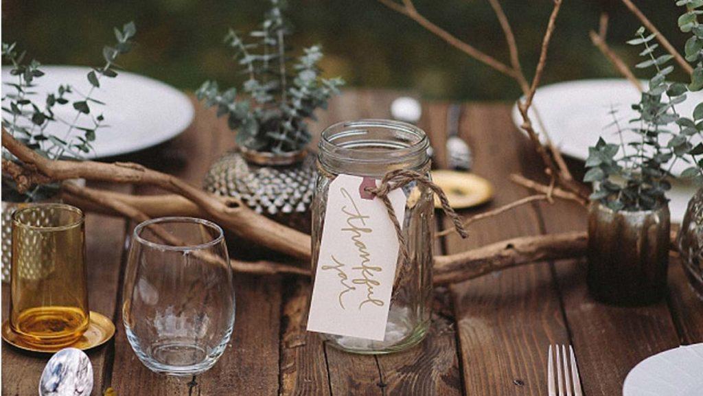 Outdoorsy Thanksgiving table decor setting with mason jar glasses, vases of plants, and branches for a centerpiece.