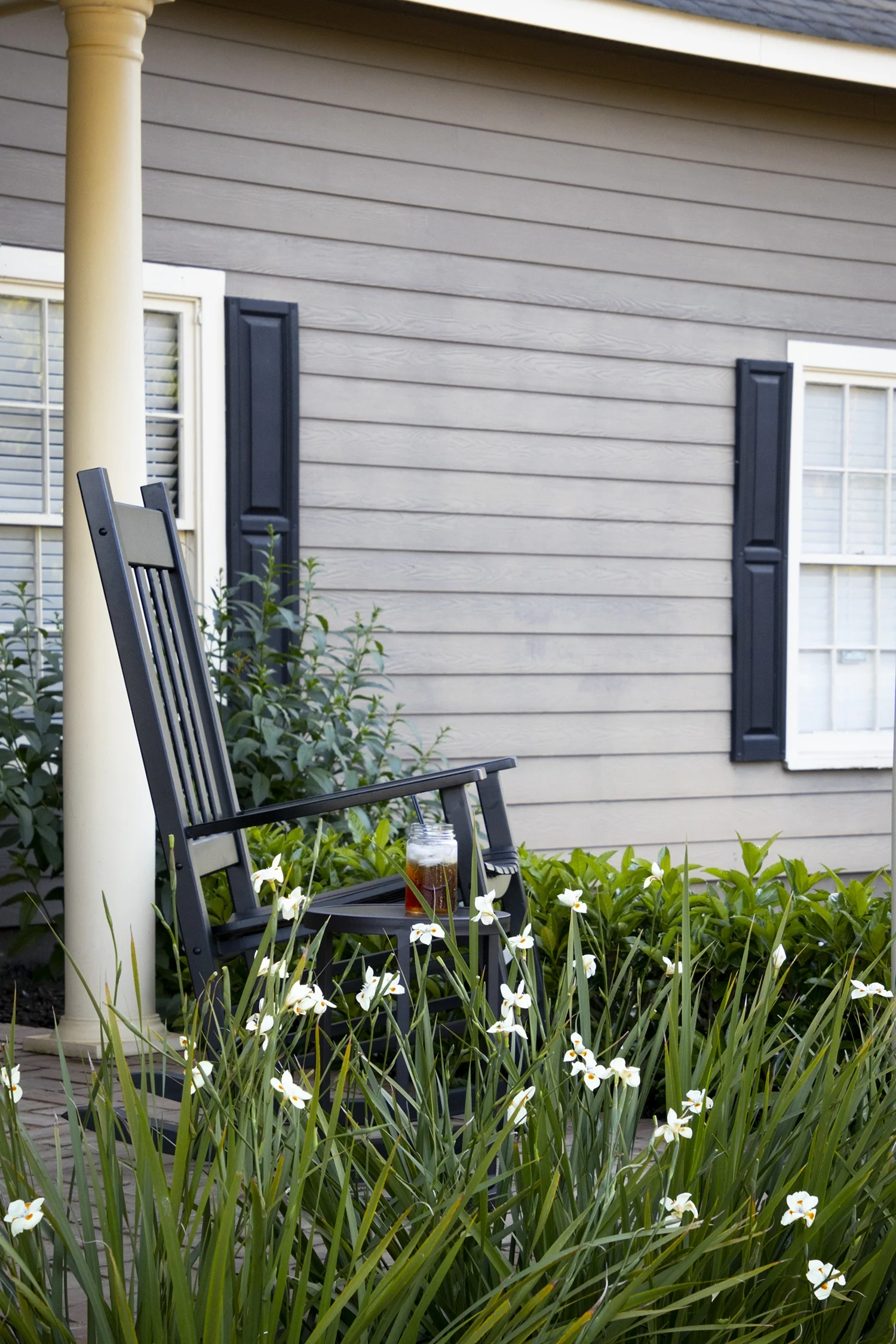 Katrina® African Iris (Dietes x 'NOLA alba') in full bloom along a residential porch foundation, displaying upright green sword-like foliage with white flowers clustered in the foreground, demonstrating mature landscape use in a cottage-style border planting.