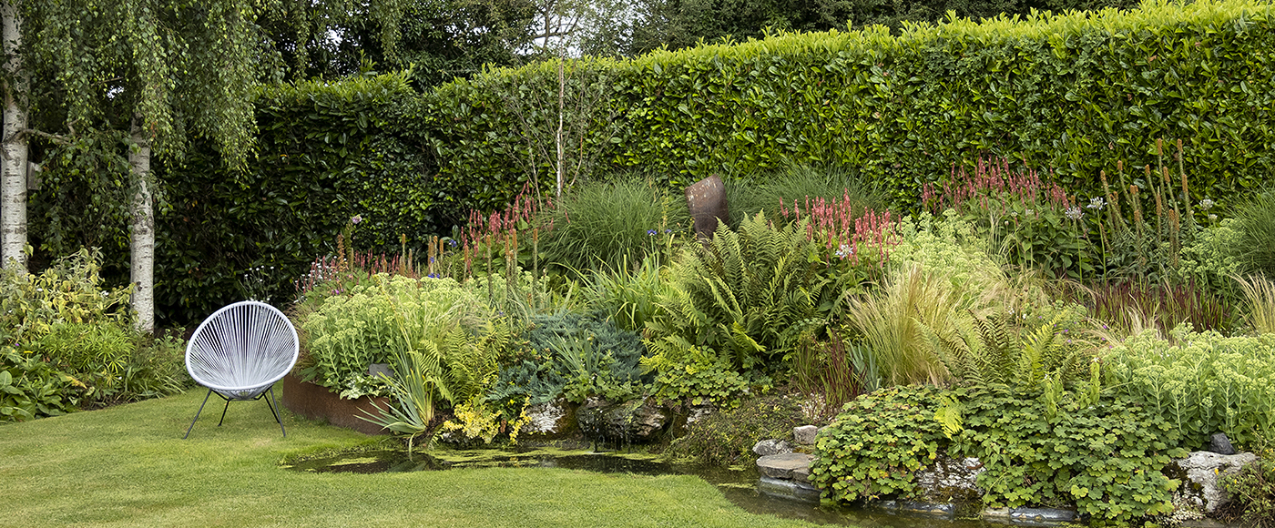 a lush rain garden setting with a gray chair next to a small pond