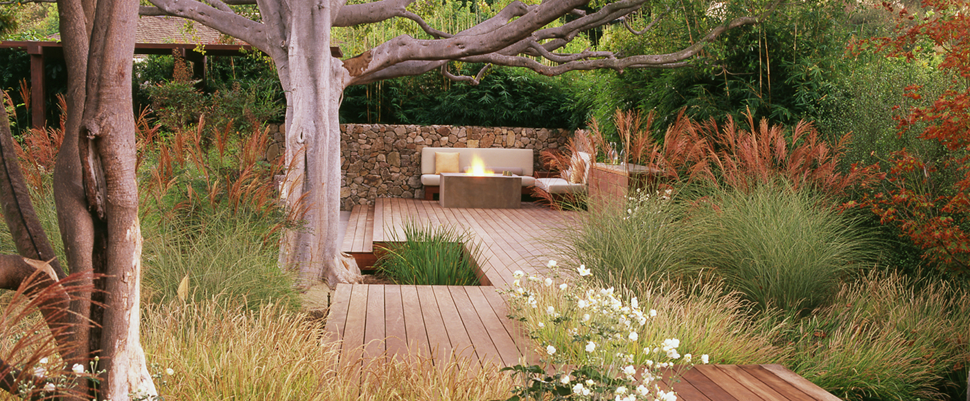 ornamental grasses surround a raised outdoor deck with outdoor living space and fire pit