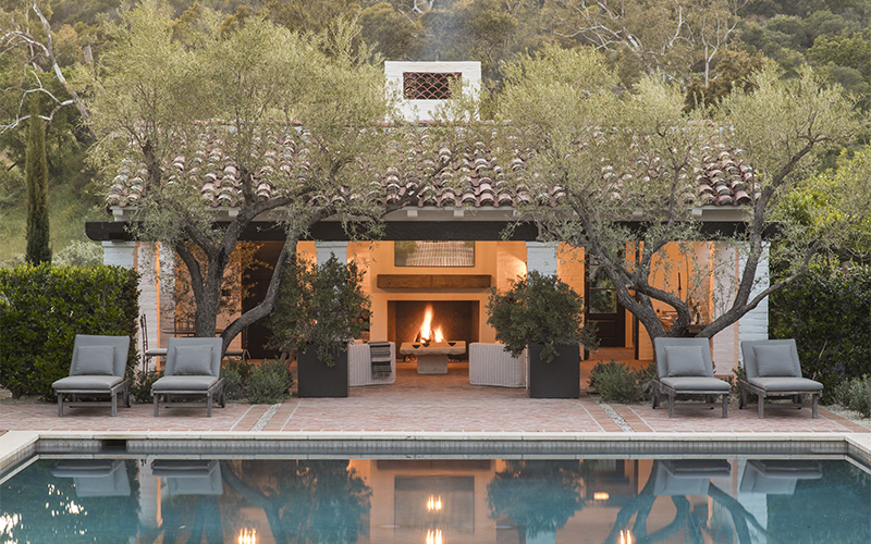 outdoor fireplace in open-air poolhouse with pool in front