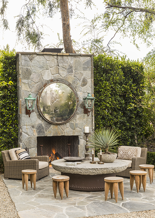 outdoor fireplace with stone slab coffee table, wooden stools and lounge chairs in front