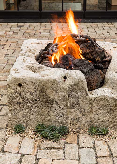 A reclaimed stone well repurposed as a cozy firepit is the centerpiece of a courtyard garden next to succulents.