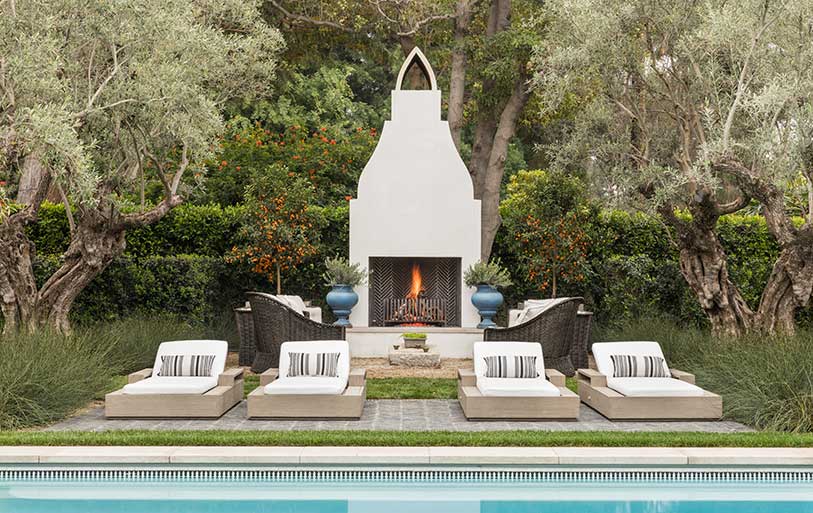 Poolside Moorish-inspired fireplace surrounded by olive trees and outdoor furniture.